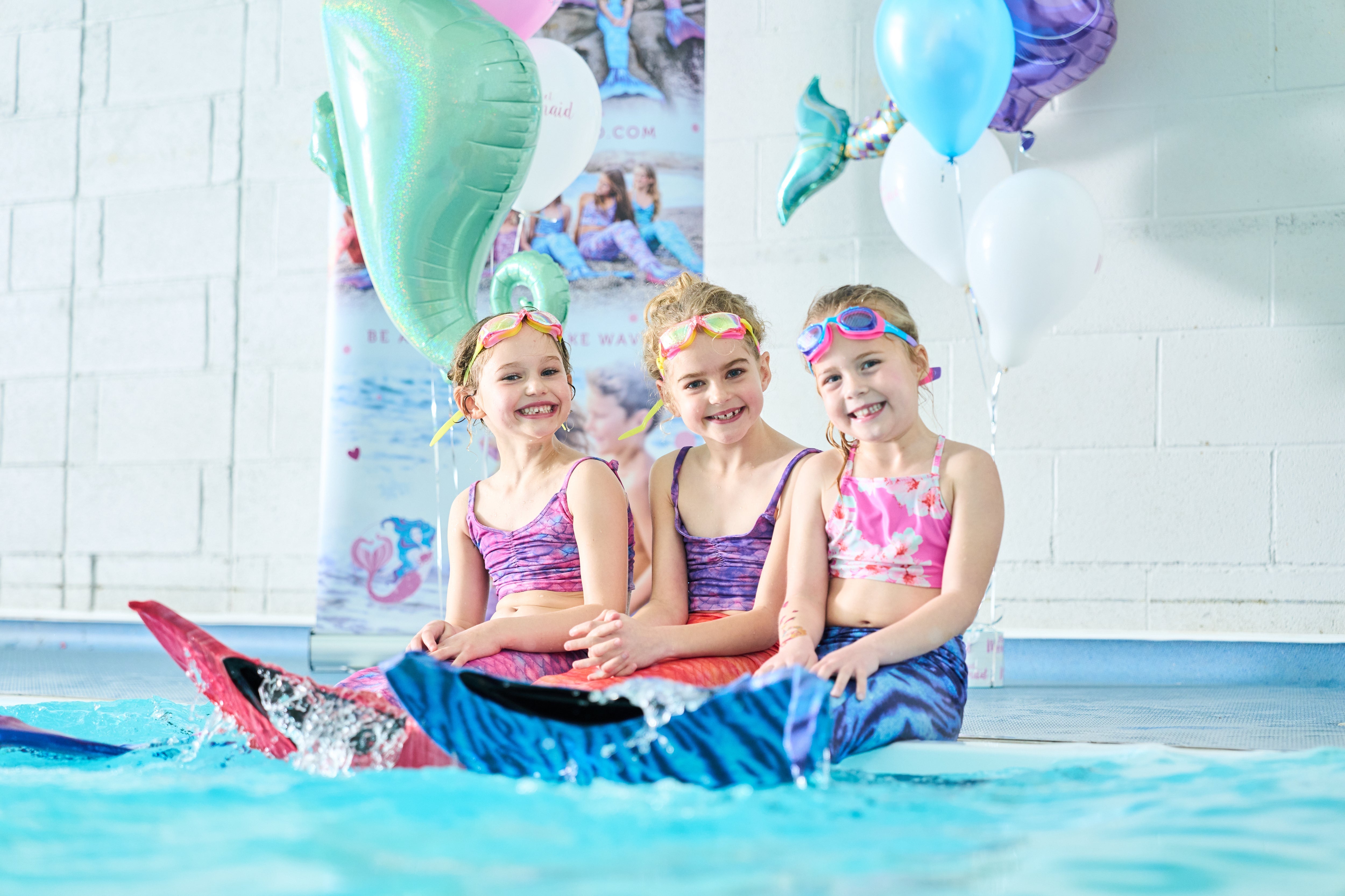 Children practising mermaid swimming with monofin tails under instructor supervision in a safe pool environment